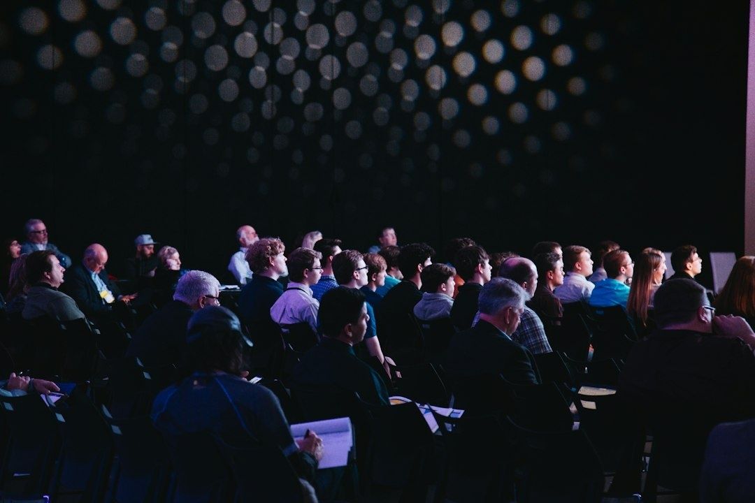 Konferenspublik sitter tillsammans i en mörk salong under ett långt möte
