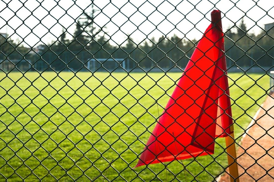 Röd markeringsflagga bakom ett stängsel vid en gräsplan