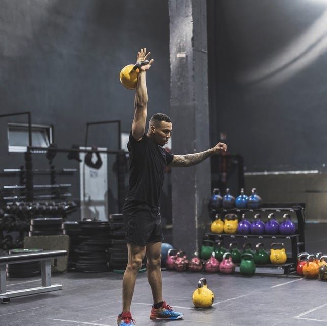 Person tränar med en kettlebell i en gymmiljö med flera vikter